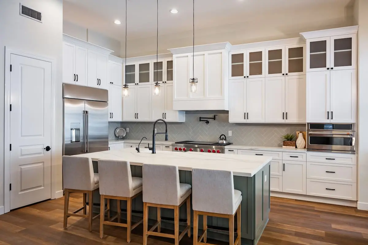 updated kitchen with white cabinets and light sage colored island and white countertops