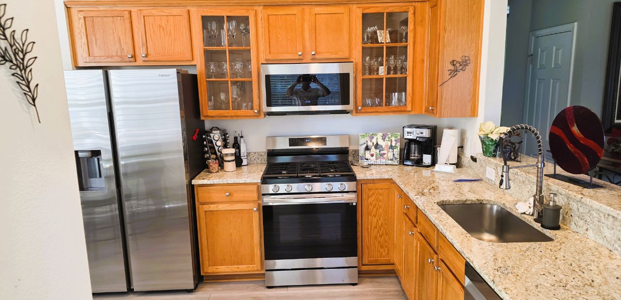 The original kitchen featured traditional oak cabinetry with a warm, golden tone that, while well-maintained, gave the space a heavier and more dated feel. The cabinet layout stopped short of the ceiling, leaving unused space above and visually compressing the room. Granite countertops with busy patterning competed for attention, while limited lighting left portions of the workspace feeling dim. The overall aesthetic leaned traditional, with mixed finishes and minimal visual cohesion.
