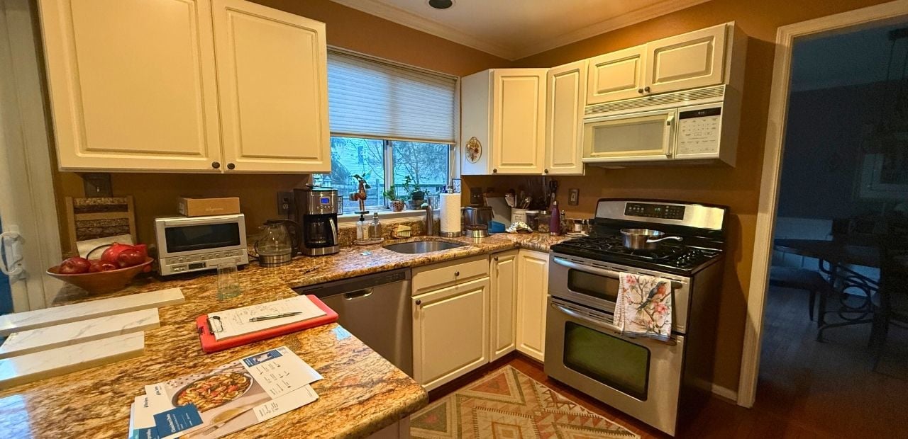 Before: U-shaped Olney kitchen with cream raised-panel cabinets, busy brown granite, mustard walls, over-range microwave, and limited storage.