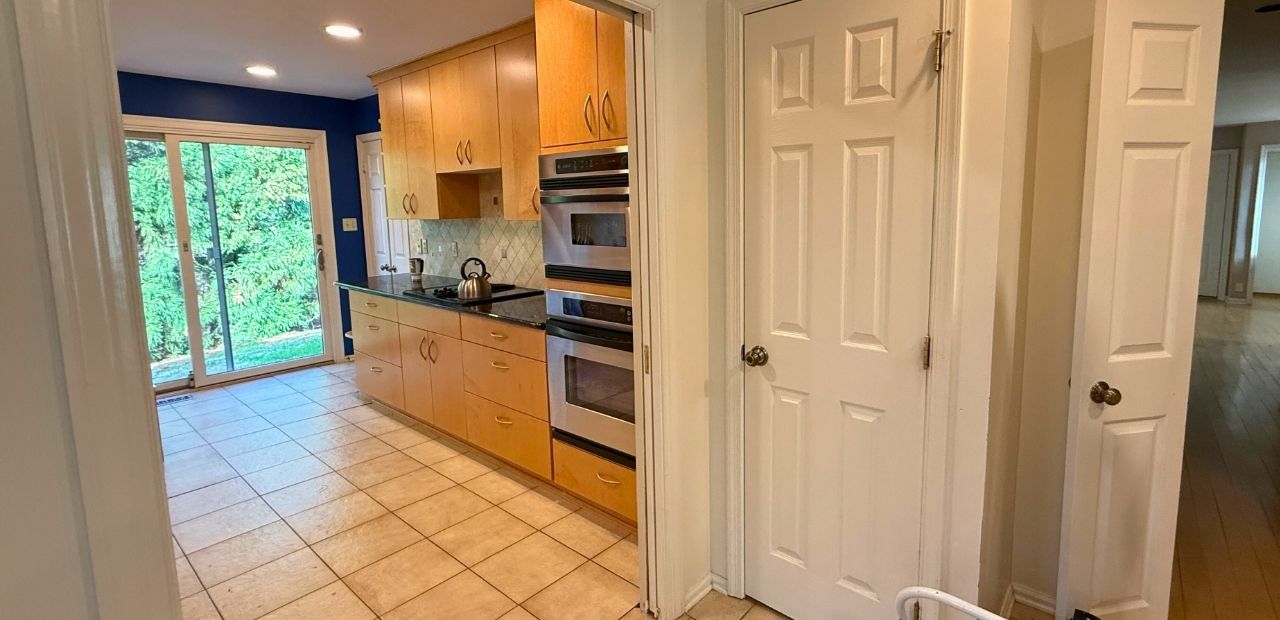 Before: Narrow galley kitchen in North Bethesda with maple slab (flat-panel) cabinets, black granite countertop, diamond-pattern tile backsplash, ceramic tile floor, and dark blue accent wall.