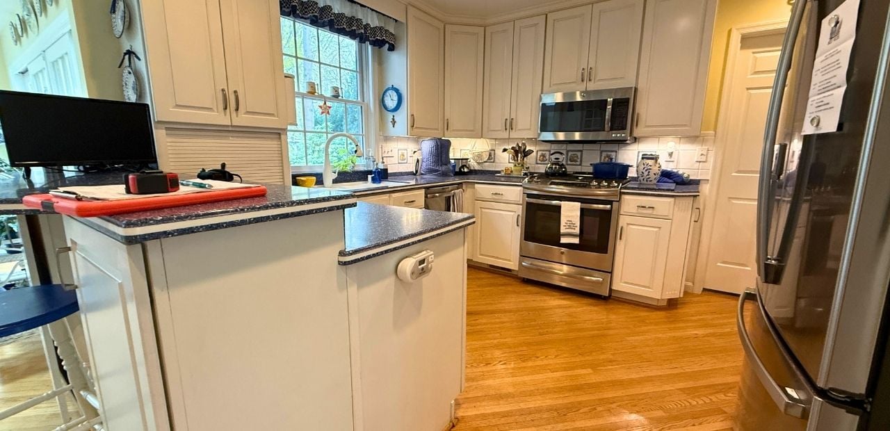 Before: Rockville kitchen with cream raised-panel cabinets, speckled blue laminate counters, two-tier bar-top peninsula, brushed-nickel pulls, and dated tile backsplash.