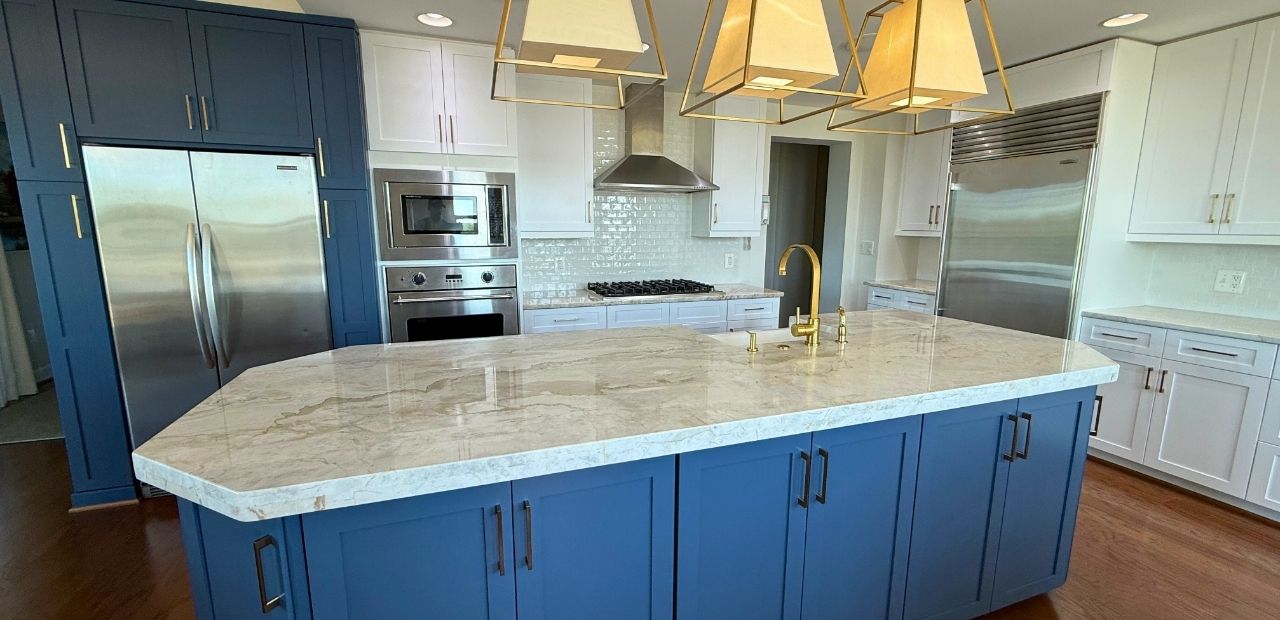 After: Same kitchen refreshed with painted-maple Mission (Shaker) doors—Satin White wall cabinets, Van Deusen Blue base and pantry units, satin-bronze pulls and faucet, original stone counters and glass backsplash retained for a luxurious two-tone statement.