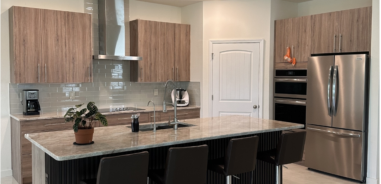 Modern kitchen in Kissimmee FL with slab cabinets, Taj Mahal quartzite island, stainless steel hood and built-in fridge and oven design