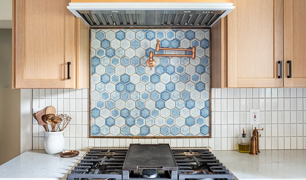 close up of hexagon tiled backsplash behind white gas stove with gold accents 