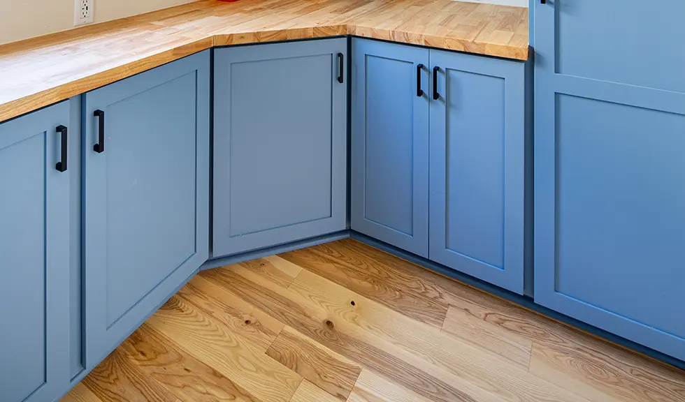 close up of blue cabinets with black handles, wood floor, and wood counter top 