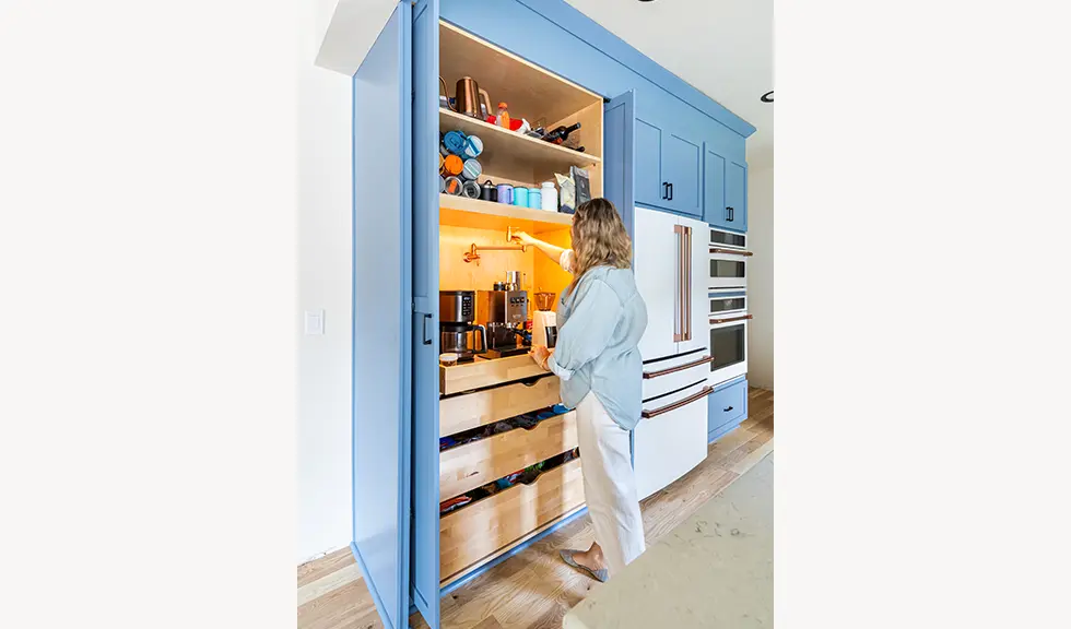 person standing in front of of the open floor to ceiling cabinet that has coffee bar and pot filler inside. 
