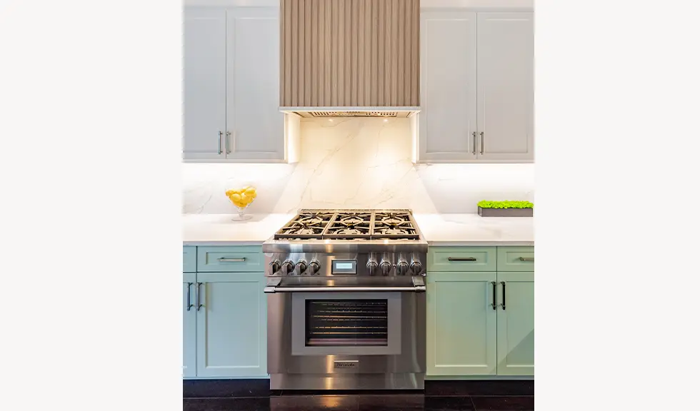 close up of stainless steel gas stove, range hood, under the cabinet lighting and two tone kitchen